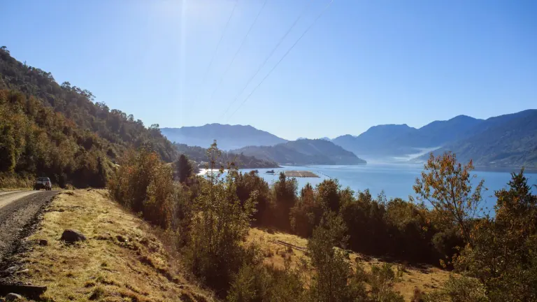 Camino de ripio junto al Estuario de Reloncaví cerca de Cochamó, con el fiordo entre cerros de bosque nativo