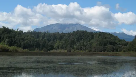 Laguna La Poza rodeada de bosque nativo, con el volcán Calbuco asomando entre nubes al fondo