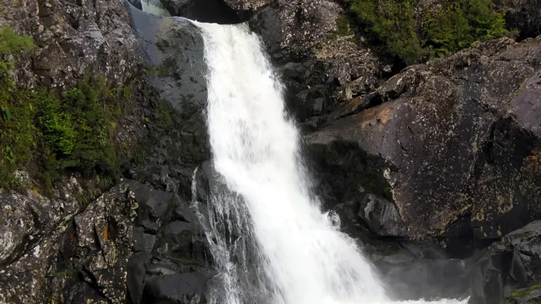 Salto del río Chaicas cayendo entre rocas oscuras y vegetación, en el sector Chaicas del Parque Nacional Alerce Andino
